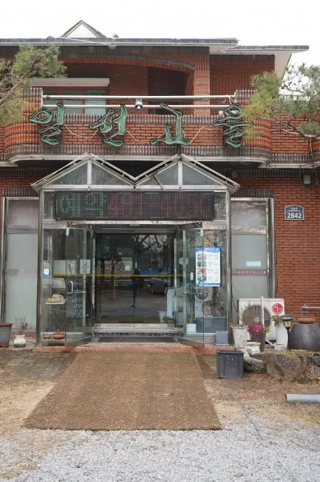 일선고을 건물 정면 — 붉은 벽돌 2층 건물과 초록 «일선고을» 간판, 소나무와 자갈 마당