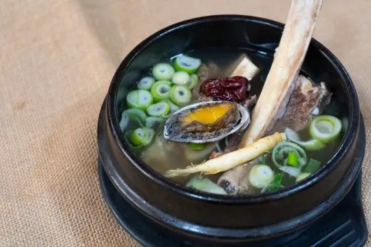 뚝배기에 담긴 탕 — 긴 뼈, 전복, 대추, 수삼, 송송 썬 대파