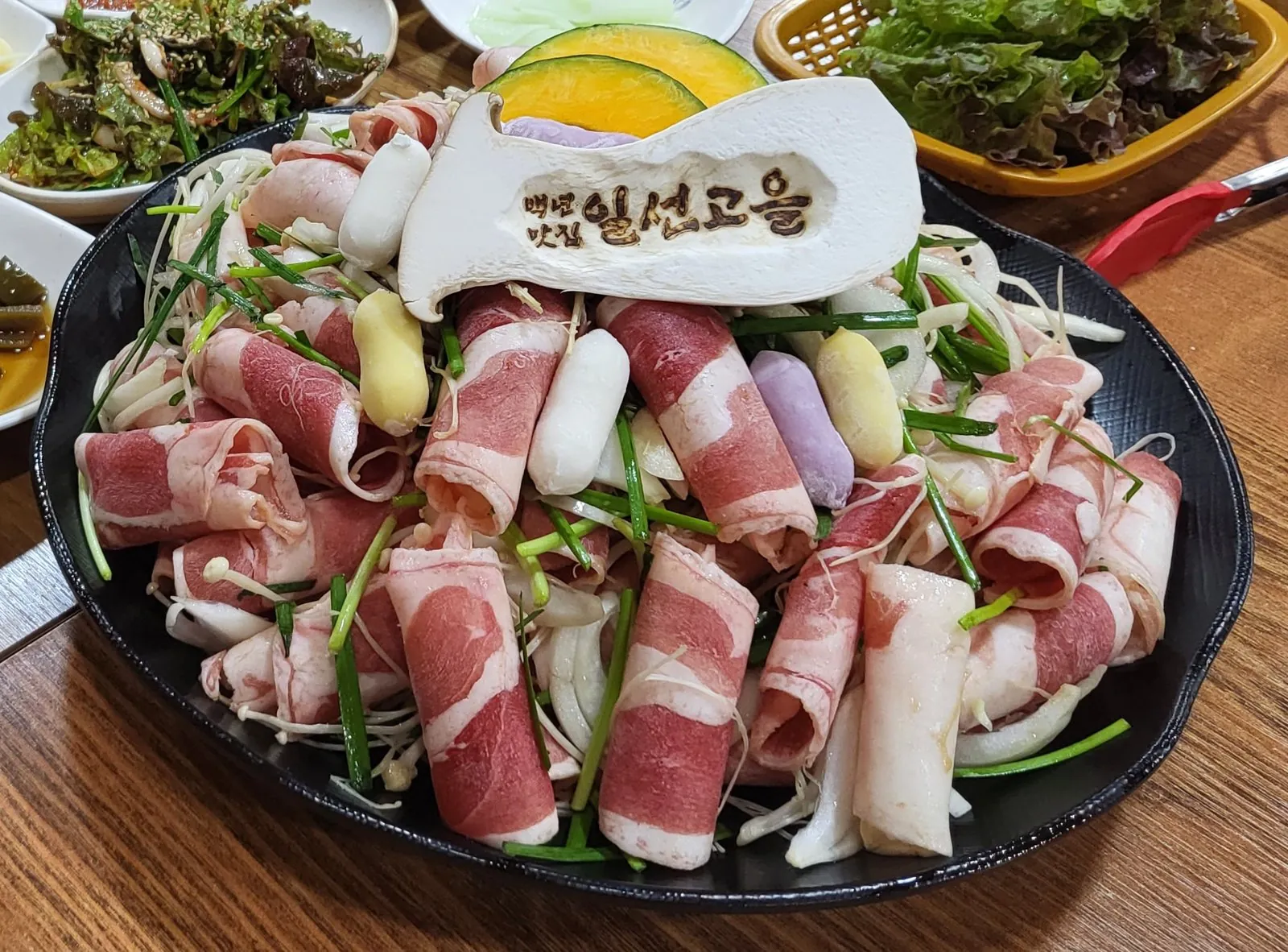 웰빙 오리불고기 — 말아 올린 오리고기 슬라이스와 부추·양파·팽이버섯, 단호박·색 떡, 일선고을 이름을 새긴 새송이버섯, 뒤로 상추 바구니와 밑반찬