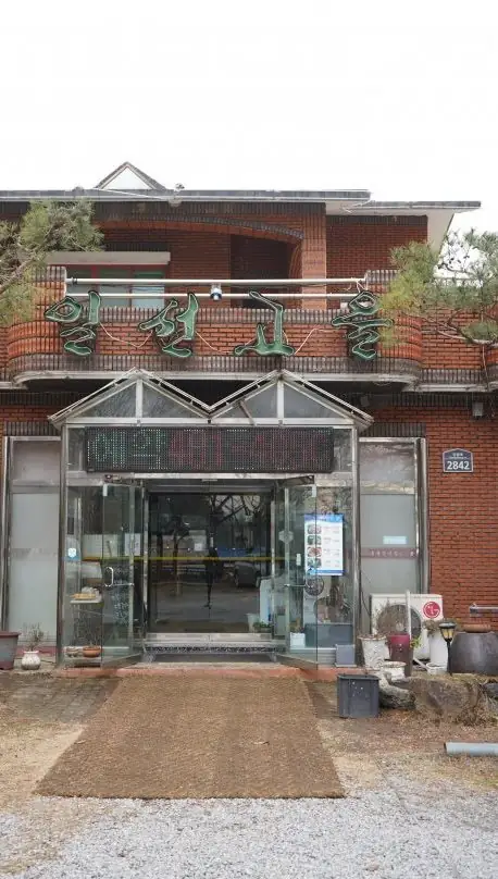 붉은 벽돌 2층 건물과 초록 간판, 소나무와 자갈 마당