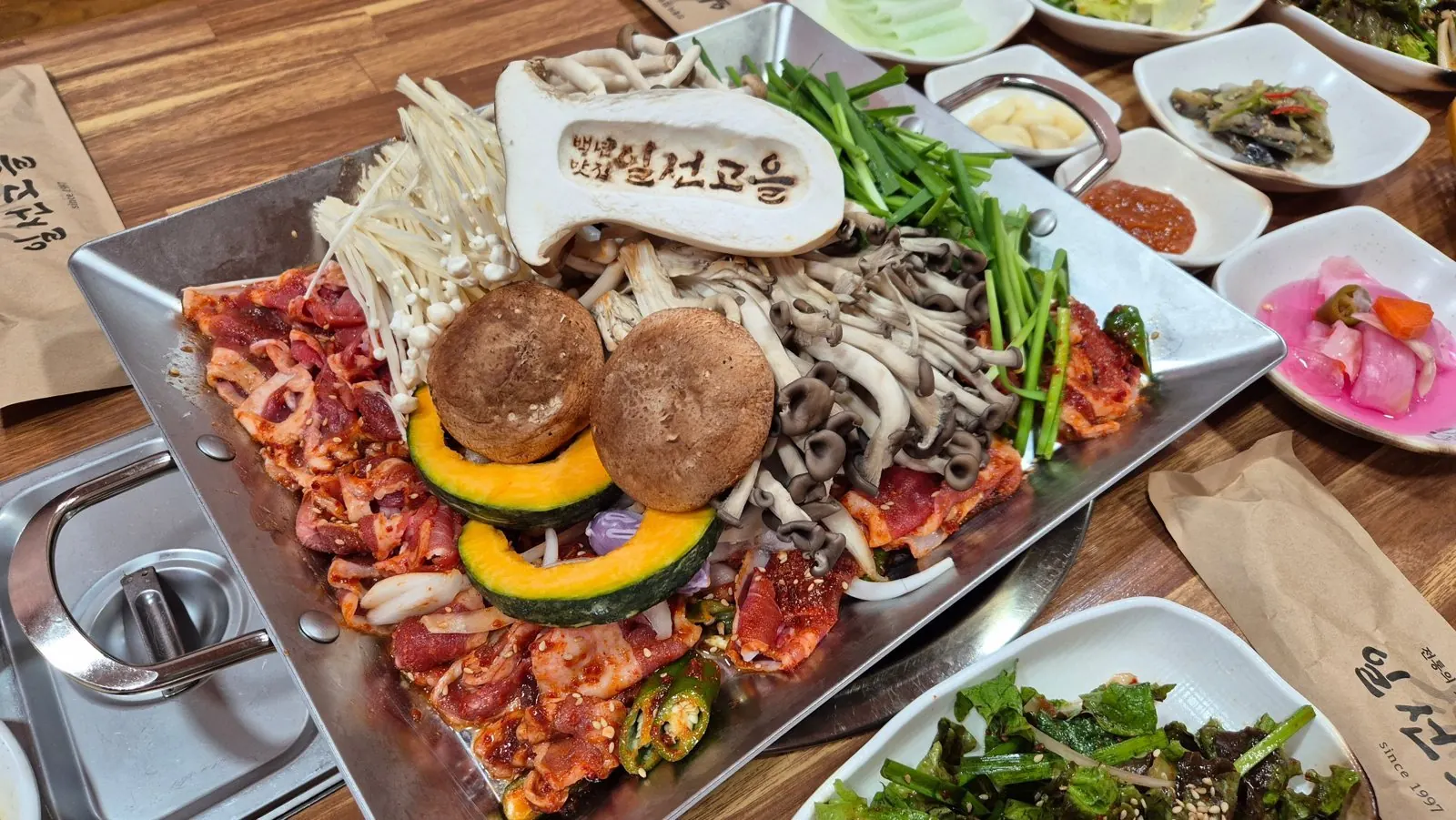 사각 팬에 담긴 버섯오리주물럭 — 붉은 양념 오리고기와 여러 가지 버섯, 단호박, 부추